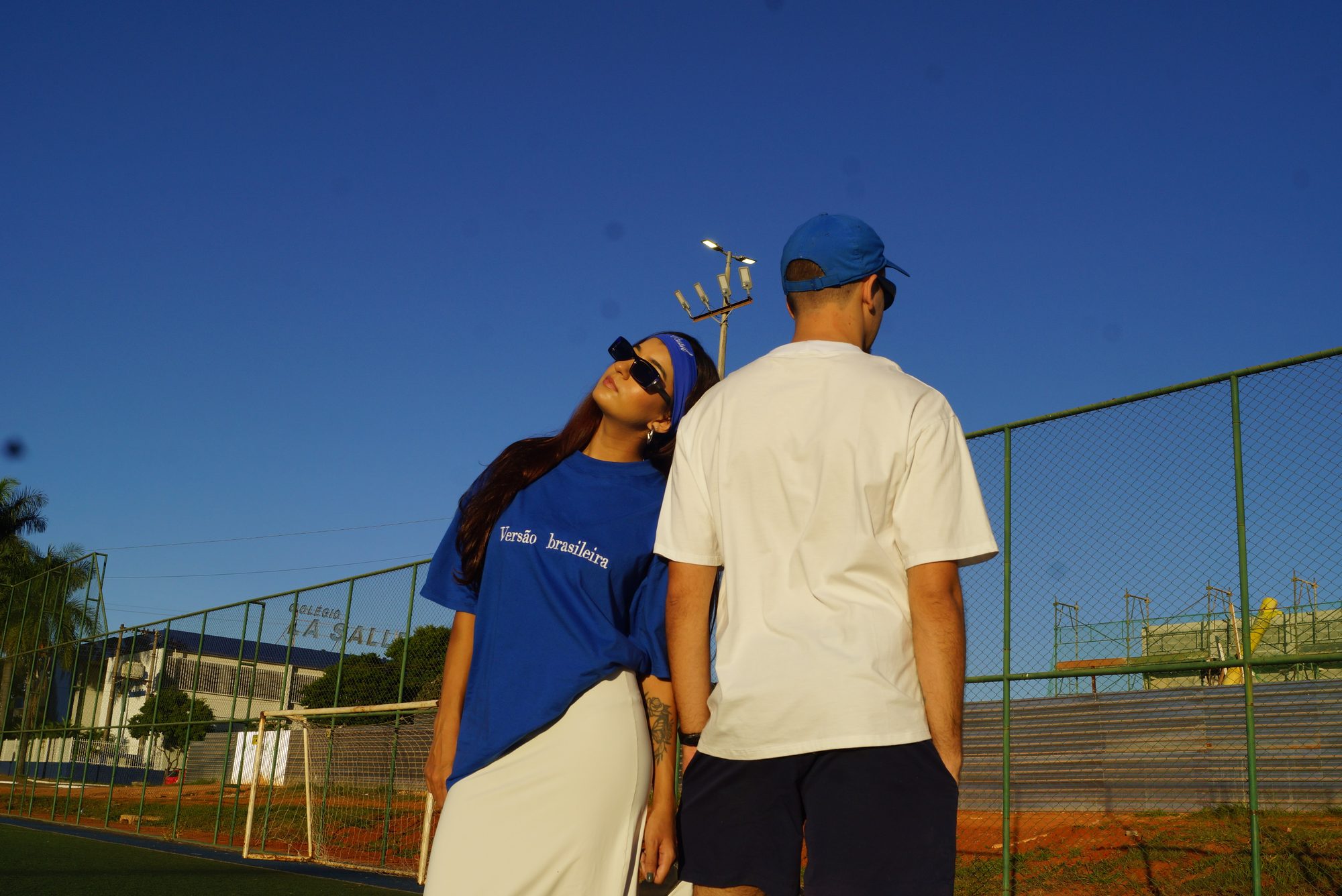 Casal em pé na quadra sob o céu azul, camiseta azul e branca