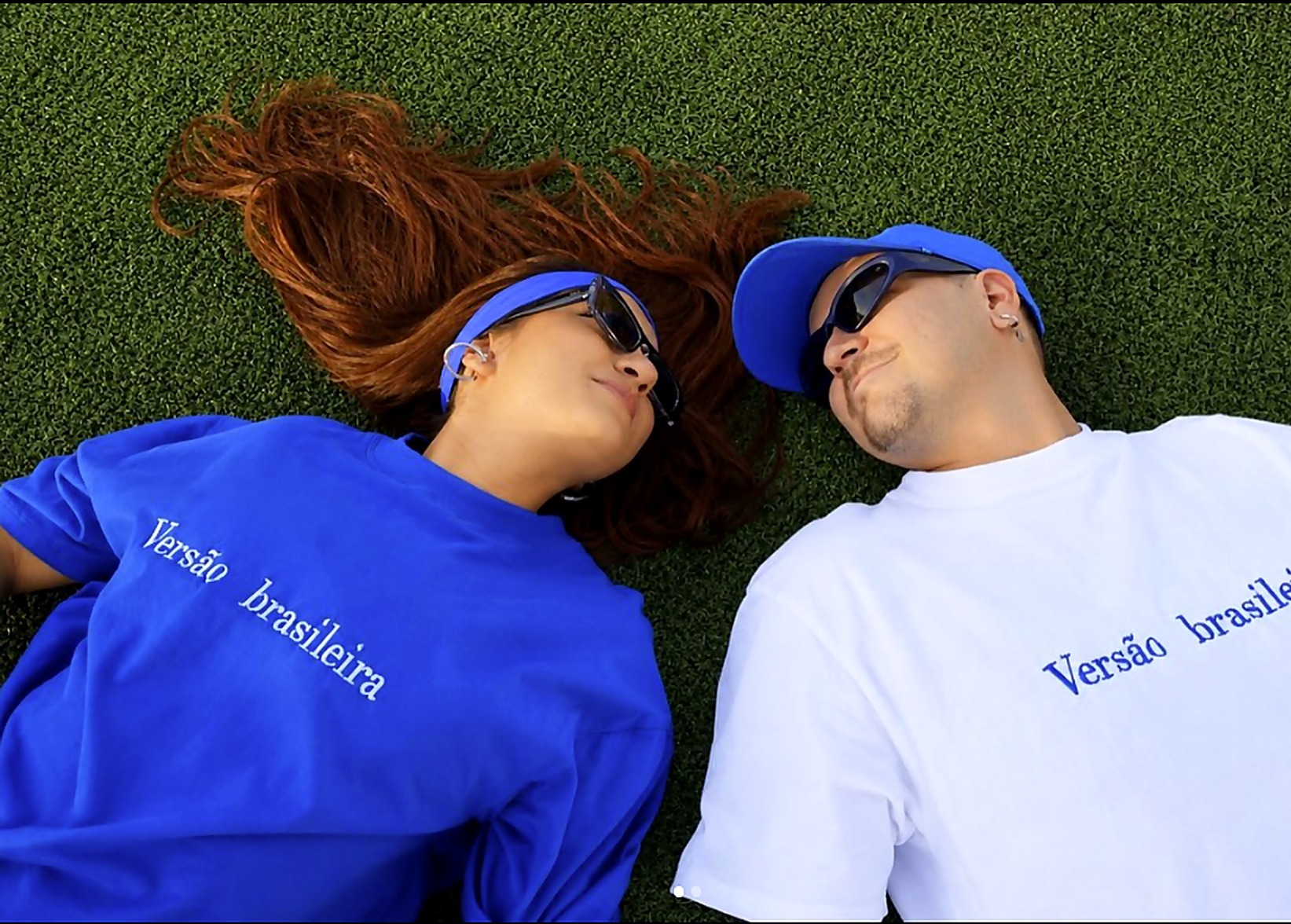 Casal deitado no gramado, cabeça com cabeça, vestindo as camisetas
